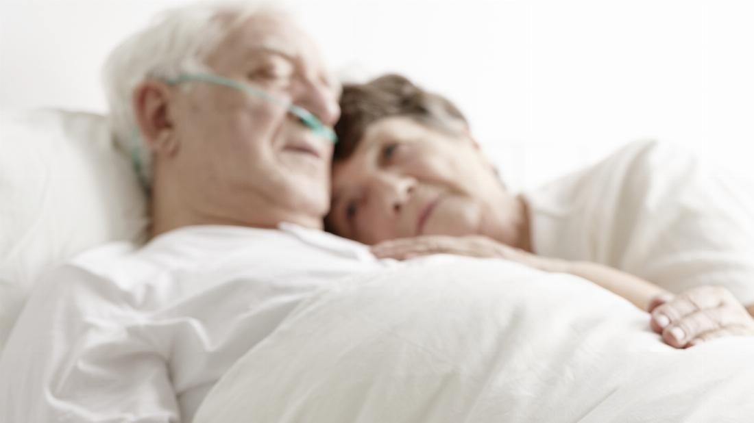 Zwei Senioren am Krankenbett. Die Frau unterstützt den schwerkranken Mann. 