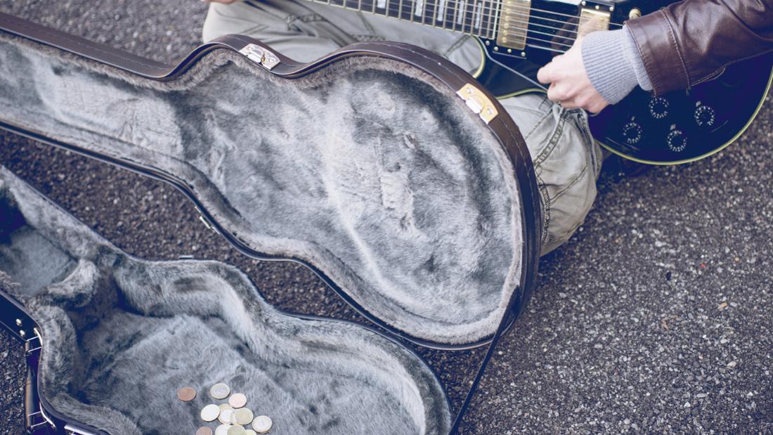Im Gitarrenkoffer eines Straßenmusikanten sind ein paar Münzen zu sehen.